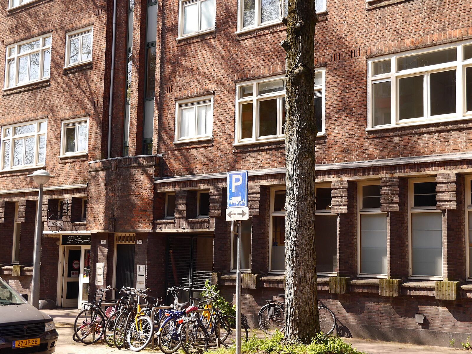 Brick apartment buildings in Nieuwe Uilenburgerstraat, Amsterdam, with bicycles parked under a tree in spring sunlight