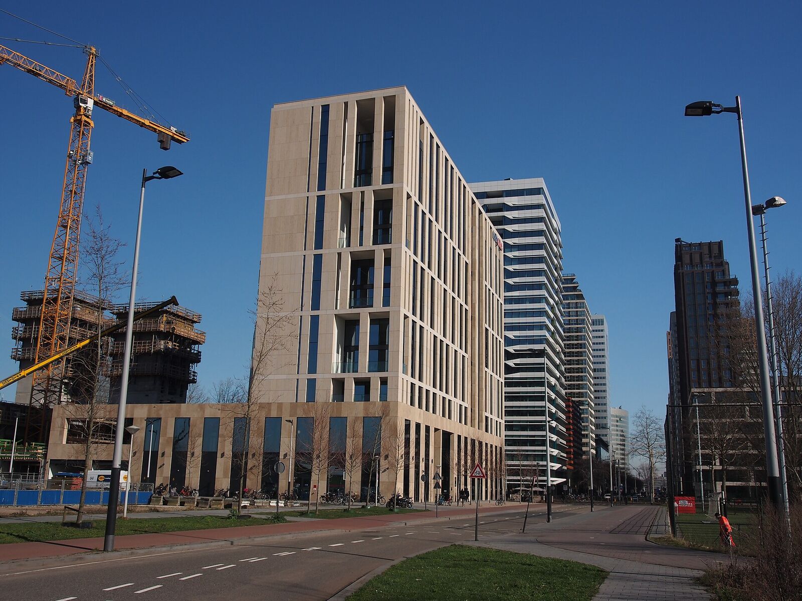 Modern office buildings with pale stone facades and glass towers along the Gustav Mahlerlaan in Amsterdam's Zuidas business district, under a blue sky