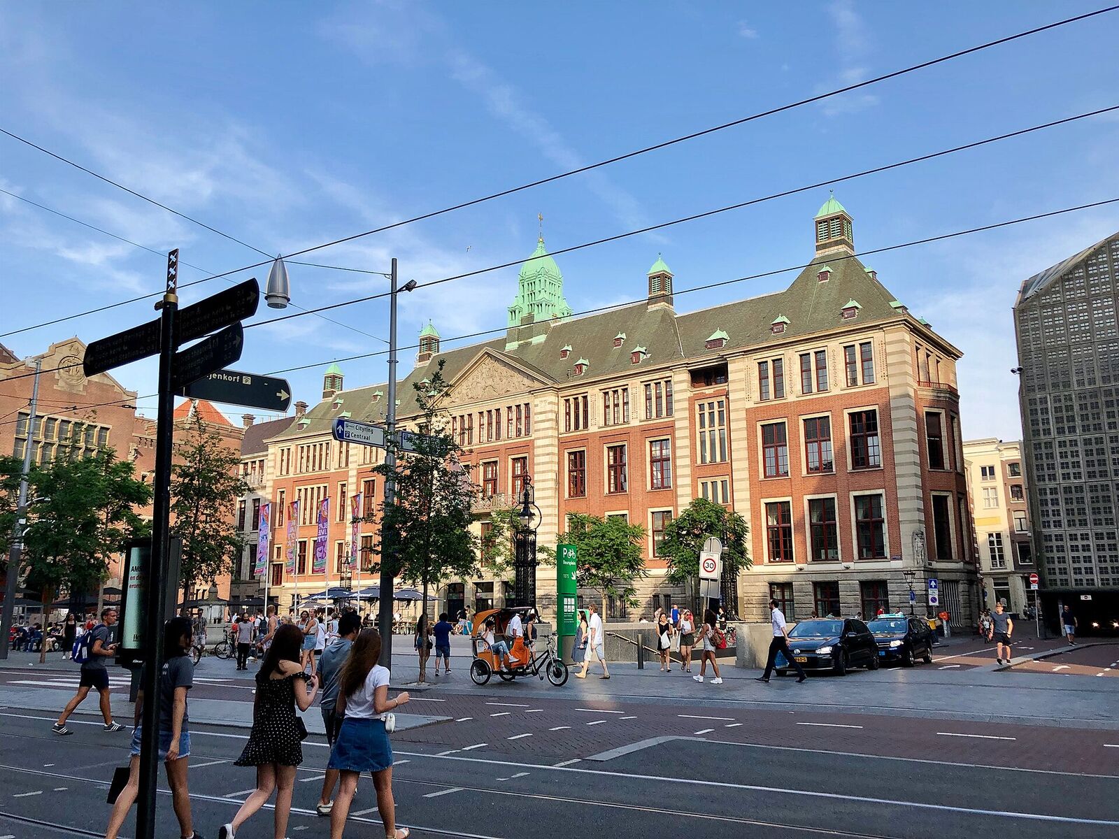 The brick and sandstone stock exchange building at Beursplein 5 in Amsterdam, with its green copper turret, on a sunny evening with tram wires overhead