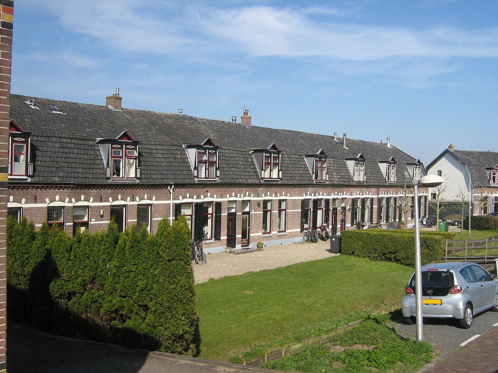 A long row of single-storey brick cottages with dormer windows and a lawn in front, on the Amsteldijk Noord in Amstelveen