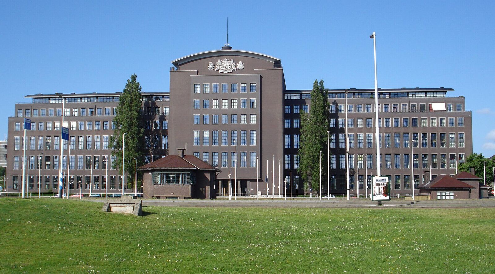 The long brown-brick former tax office on Puntegaalstraat in Rotterdam, a listed building with a coat of arms above the central tower, seen across a lawn