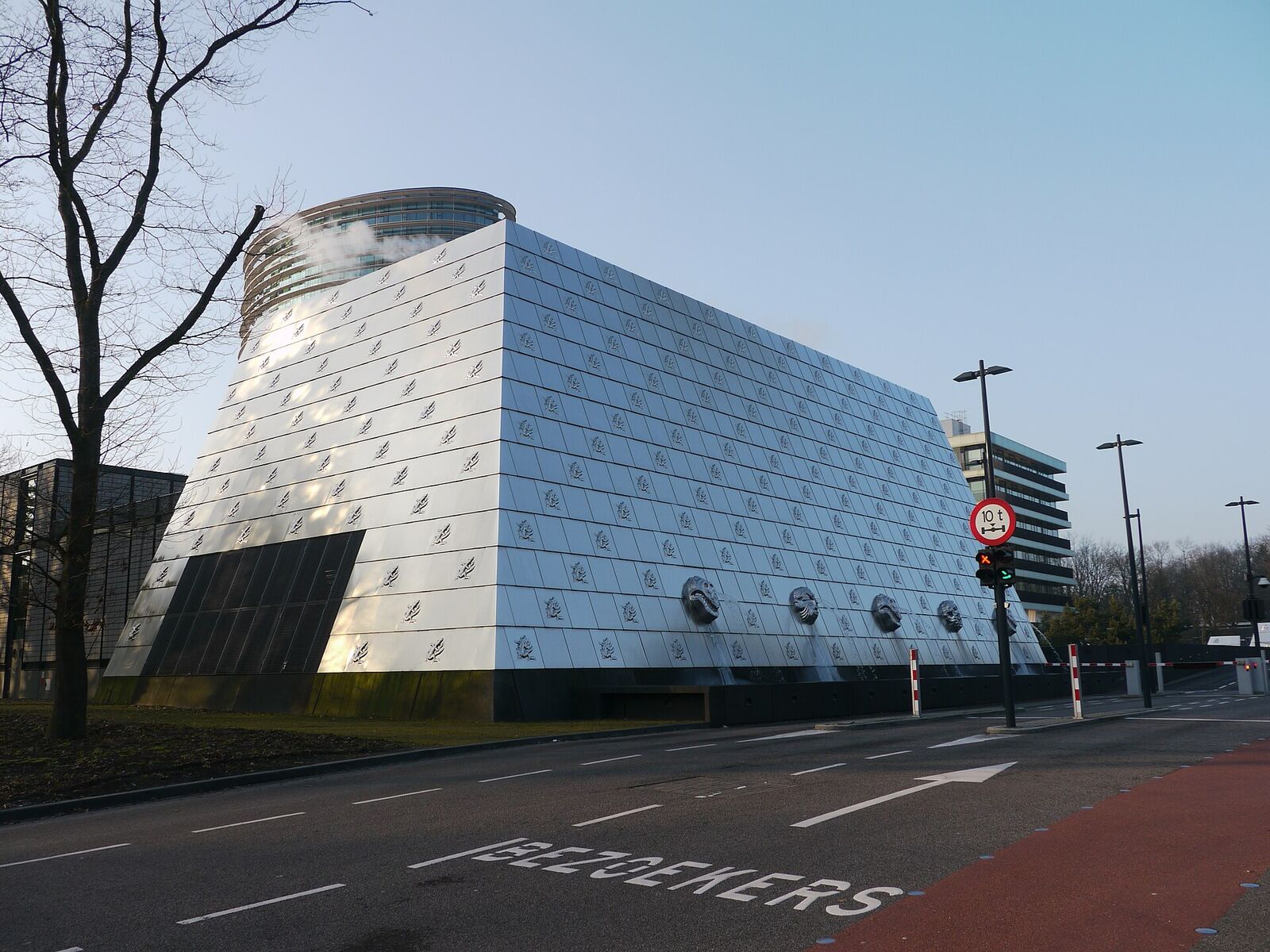 The sloping, metal-clad entrance building of the Belastingdienst tax office in Apeldoorn, with decorative reliefs on the facade and a road in front